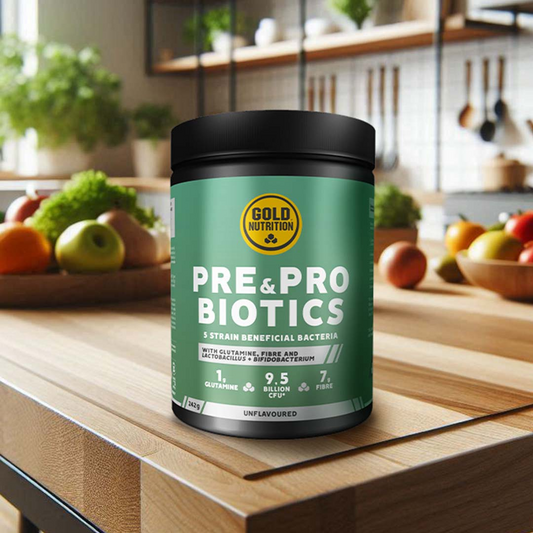 Embalagem de suplemento GoldNutrition contendo Pré-bióticos e Probióticos, com 5 estirpes de bactérias benéficas, glutamina, fibra e 9,5 bilhões de UFC. O produto está numa cozinha com frutas e vegetais ao fundo.